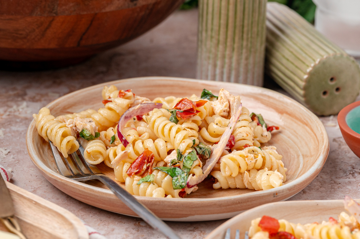 Cold chicken pasta salad with sun-dried tomatoes, basil, Parmesan, and rotini coated in a light dressing Serving of Sun-Dried Tomato Chicken Pasta Salad with rotini, basil, red onion, and rotisserie chicken on a small plate