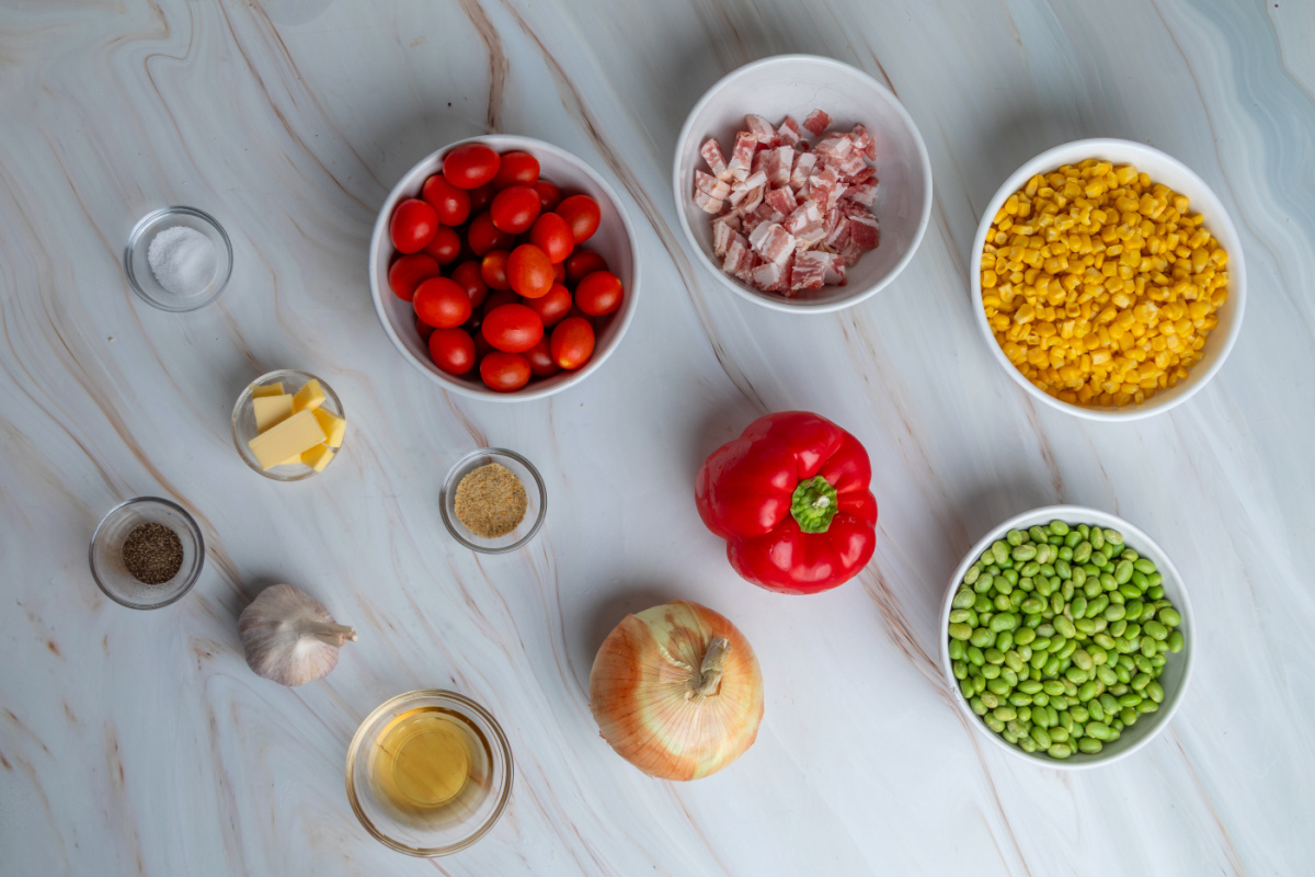Ingredients needed for corn succotash with edamame and bacon Ingredients for corn succotash including sweet corn, edamame, bacon, tomatoes, bell pepper, onion, garlic, butter, and apple cider vinegar