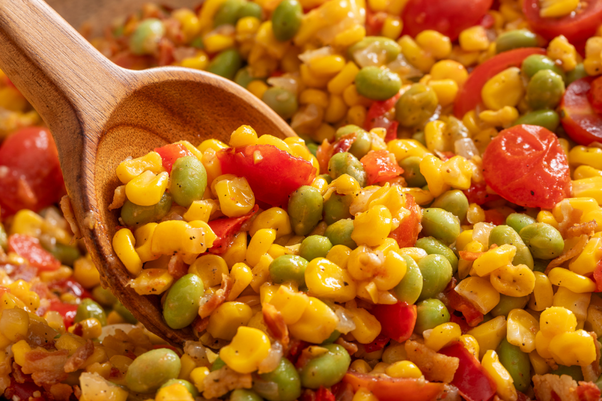 Spoonful of corn succotash with edamame and bacon Close-up spoonful of corn succotash with edamame, tomatoes, bacon, and sweet corn