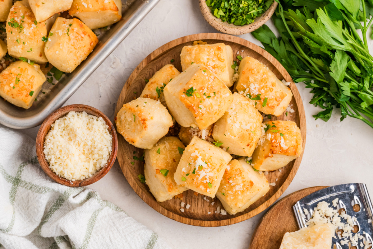 Parmesan bread bites on a wooden platter topped with Parmesan cheese and fresh parsley