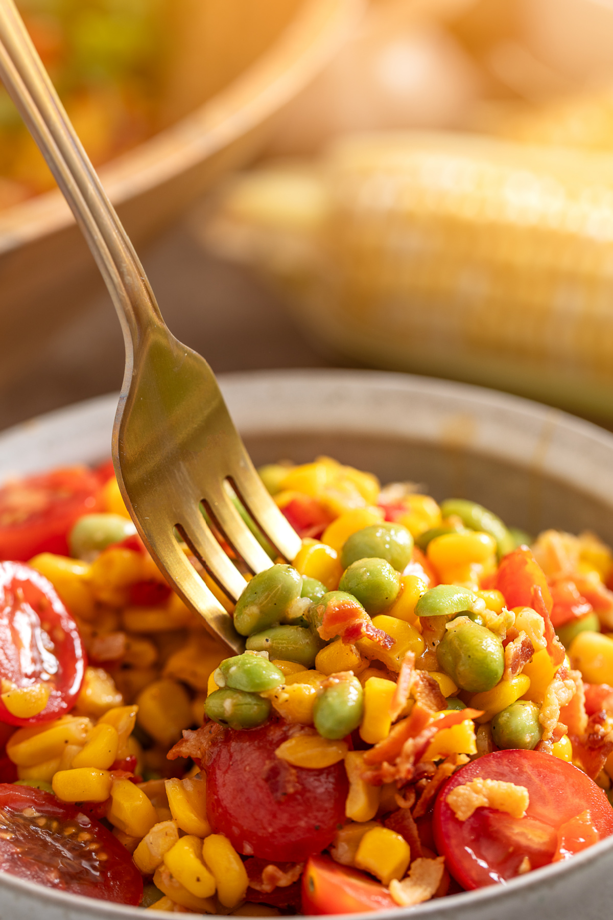 Forkful of sweet corn, edamame, bacon, and tomatoes Fork lifting sweet corn, edamame, bacon, and tomatoes from a summer vegetable side dish