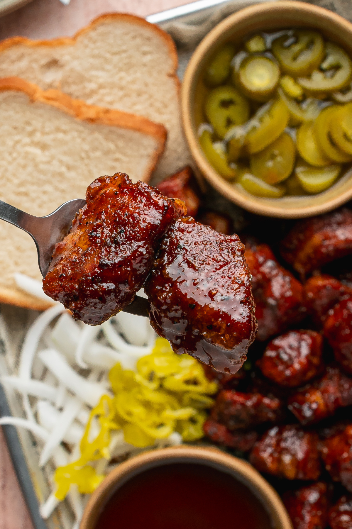 Forkful of Peach Tea Pork Belly Burnt Ends with sticky peach tea glaze. Fork holding two Peach Tea Pork Belly Burnt Ends coated in a glossy caramelized peach tea glaze.