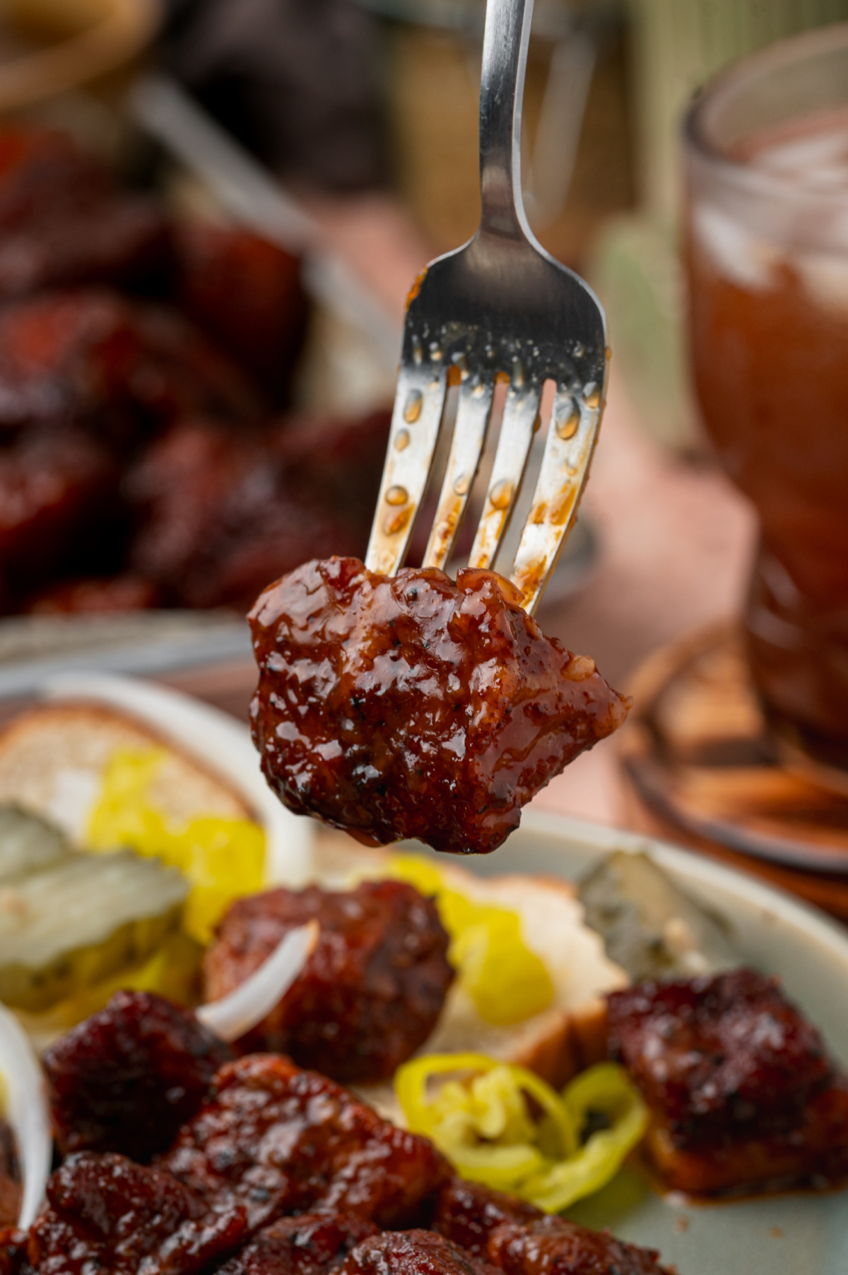 Close-up of a sticky glazed pork belly burnt end ready to eat. Close-up of a caramelized pork belly burnt end coated in glossy peach tea glaze on a fork.