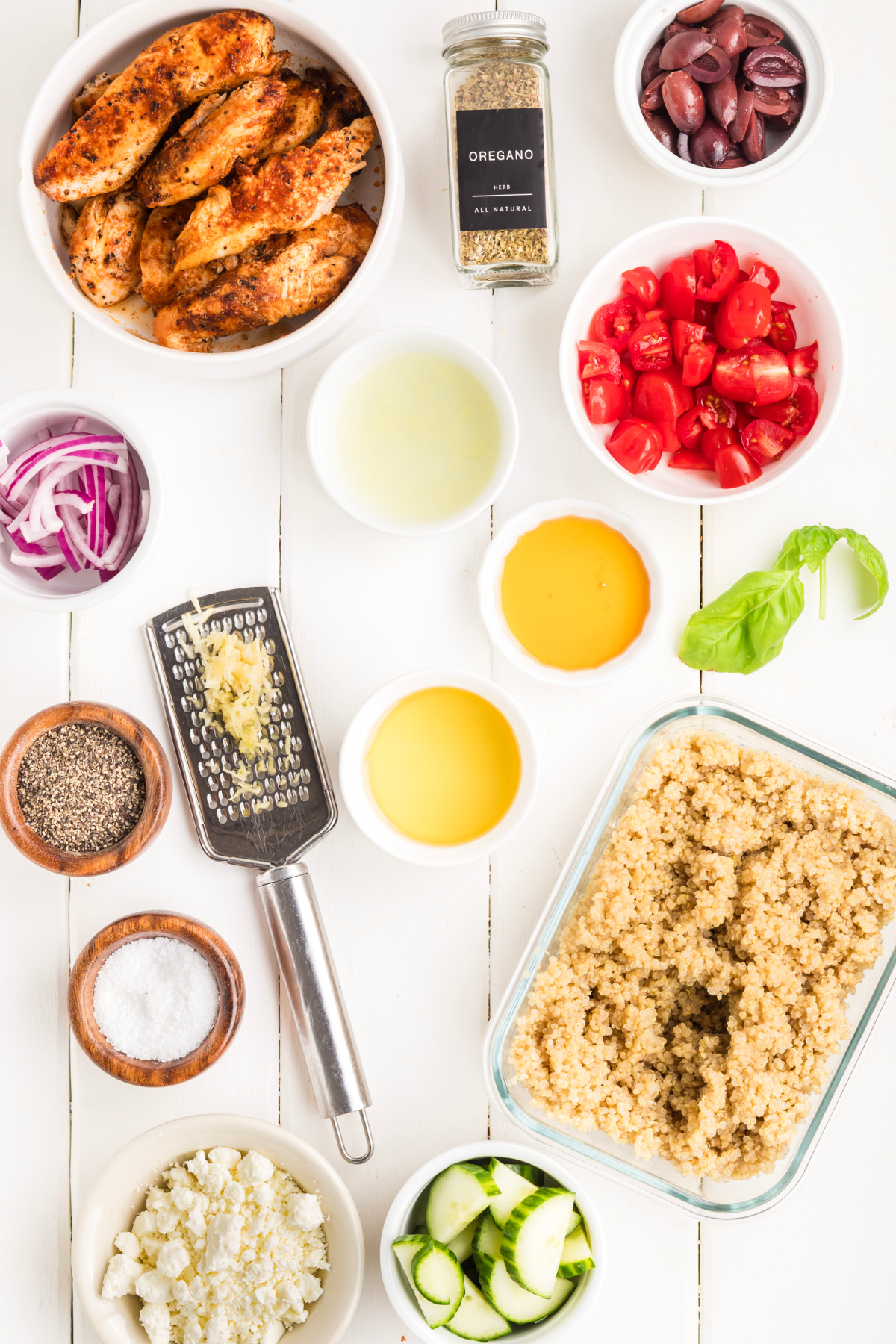Ingredients for Mediterranean chicken bowl including grilled chicken, cooked quinoa, cucumber, cherry tomatoes, Kalamata olives, feta, red onion, basil, lemon juice, olive oil, garlic, oregano, salt, pepper, and honey.