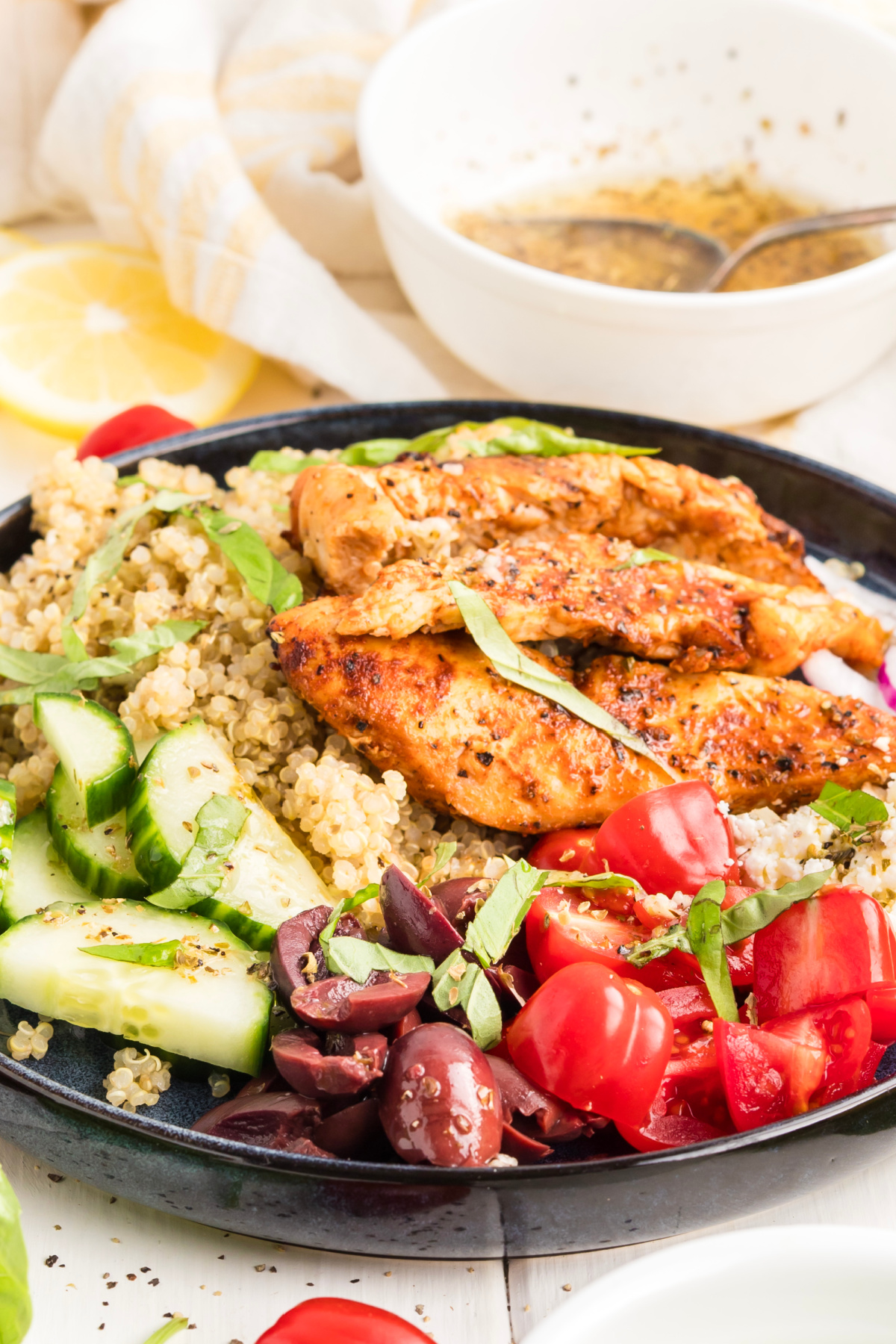 Mediterranean grilled chicken quinoa bowl with cucumber, cherry tomatoes, Kalamata olives, feta, fresh basil, and lemon vinaigrette.