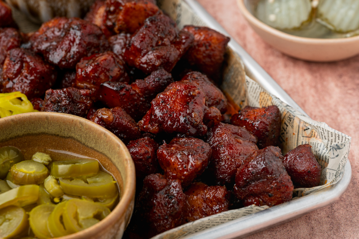 Close-up of glossy Peach Tea Pork Belly Burnt Ends fresh from the oven. Close-up of Peach Tea Pork Belly Burnt Ends coated in a sticky caramelized peach tea glaze with sliced pickled jalapeños.