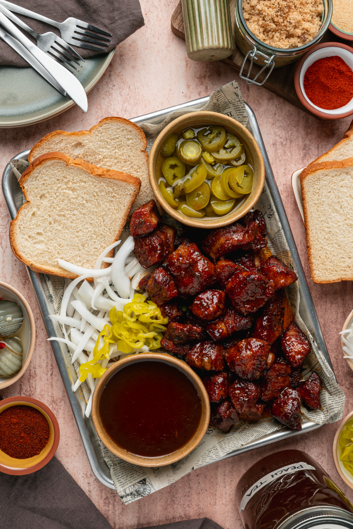 Peach Tea Pork Belly Burnt Ends served with classic barbecue sandwich fixings. Peach Tea Pork Belly Burnt Ends served on a tray with sliced bread, pickled jalapeños, onions, and extra peach tea glaze.