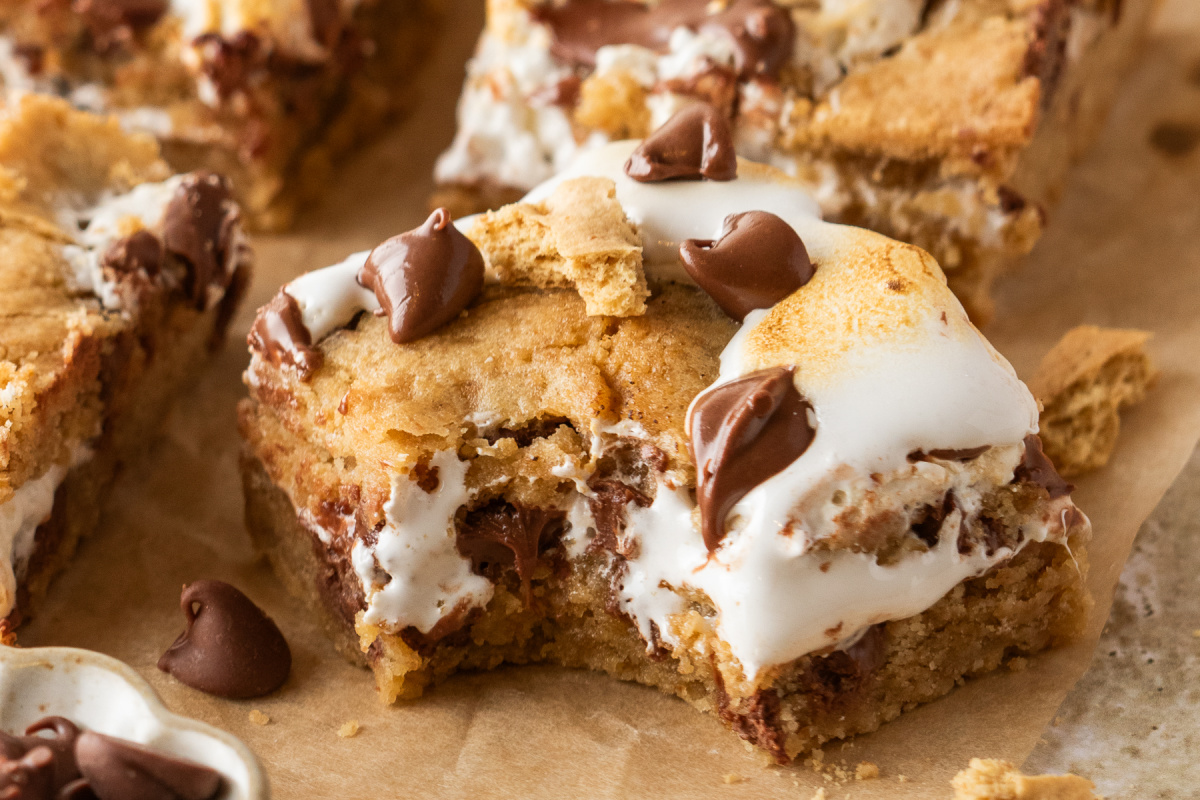 S'mores Cookie Bars with Marshmallow Creme S'mores cookie bars with graham cookie dough, gooey marshmallow creme filling, and milk chocolate chips.