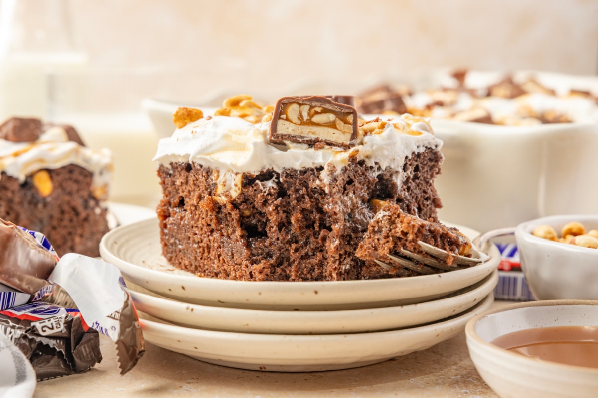 Chocolate cake slice showing pudding and caramel filling beneath whipped topping and chopped Snickers