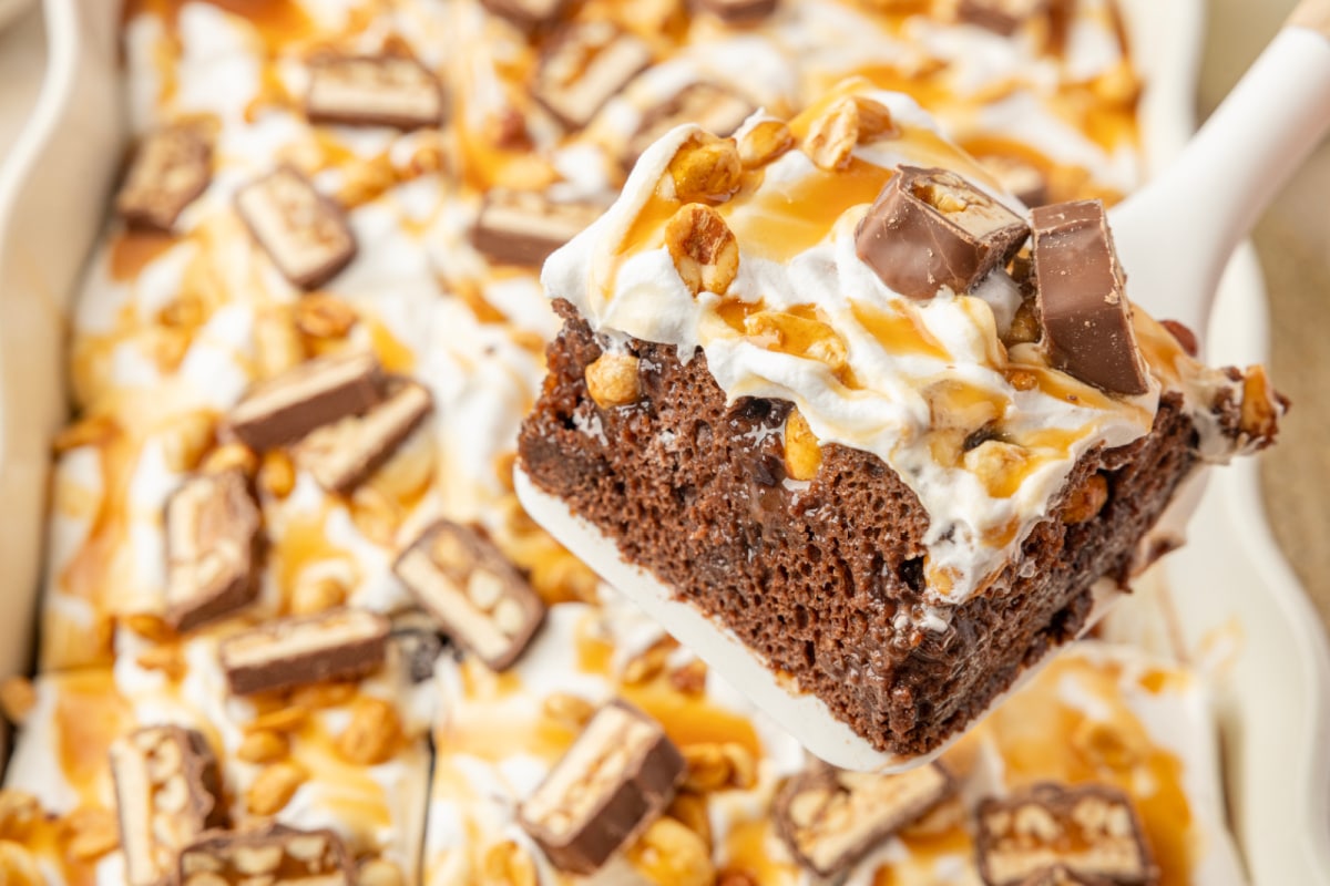 Chocolate poke cake slice showing pudding and caramel filling with roasted salted peanuts