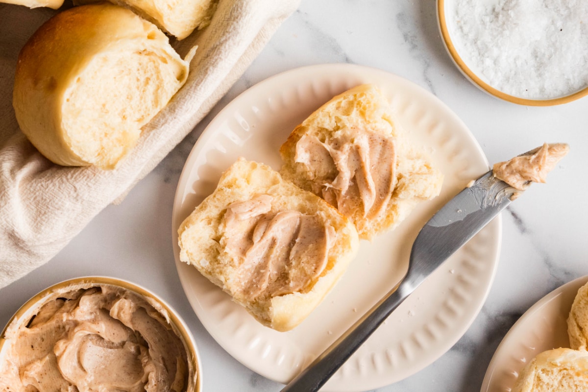 Soft dinner rolls served with cinnamon maple butter Split homemade dinner rolls spread with cinnamon maple butter on a plate.