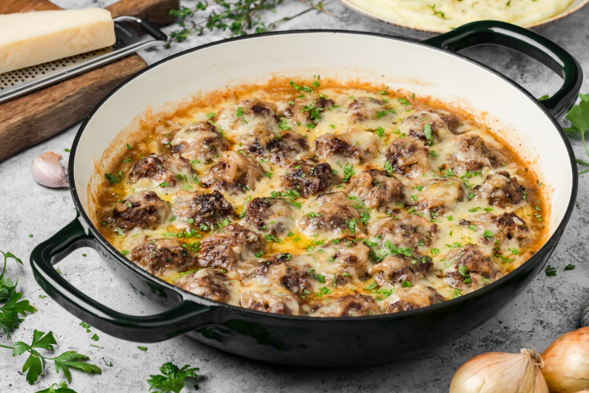 French onion meatballs with caramelized onions and melted Gruyère in a skillet