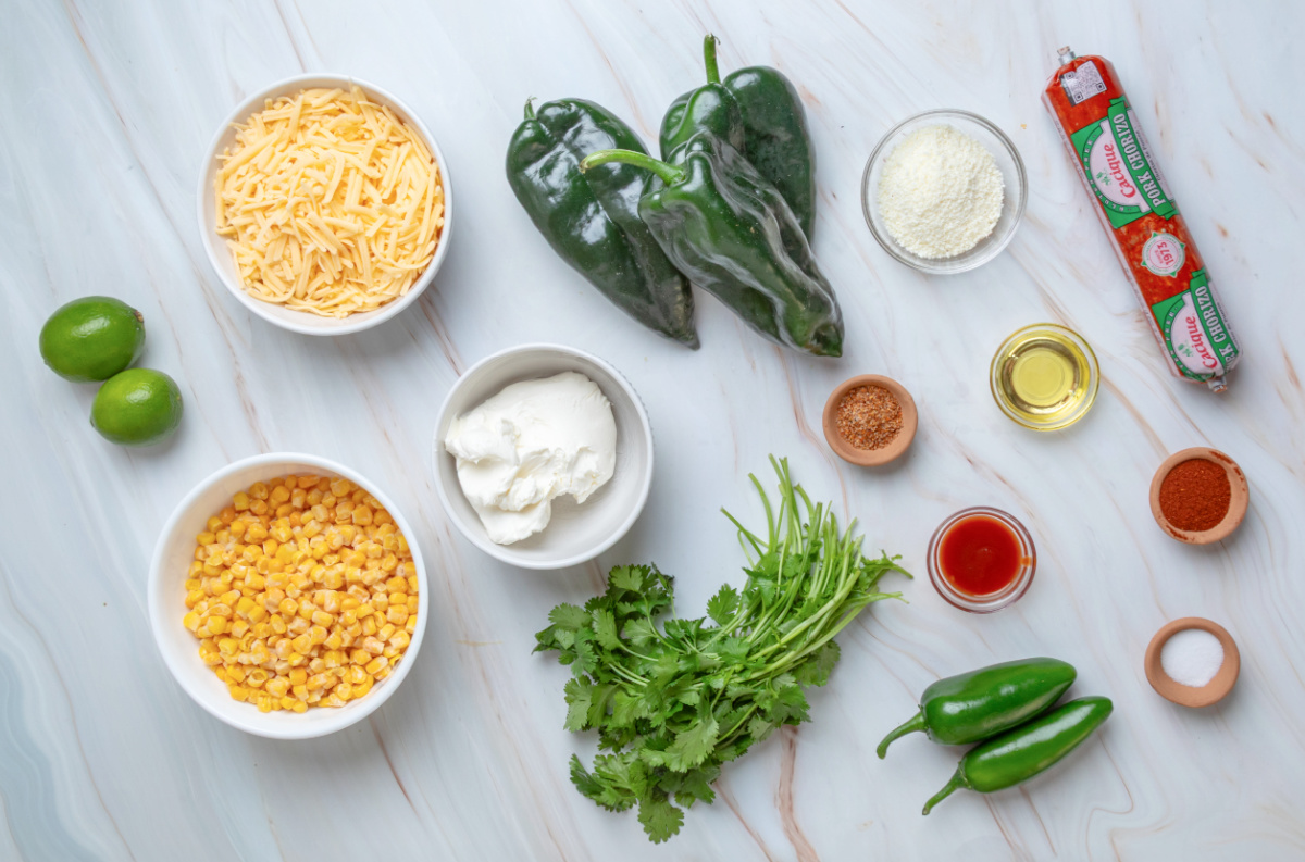 Ingredients for Mexican street corn stuffed poblano peppers including poblanos, corn, chorizo, cream cheese, shredded cheese, Cotija, jalapeños, cilantro and lime