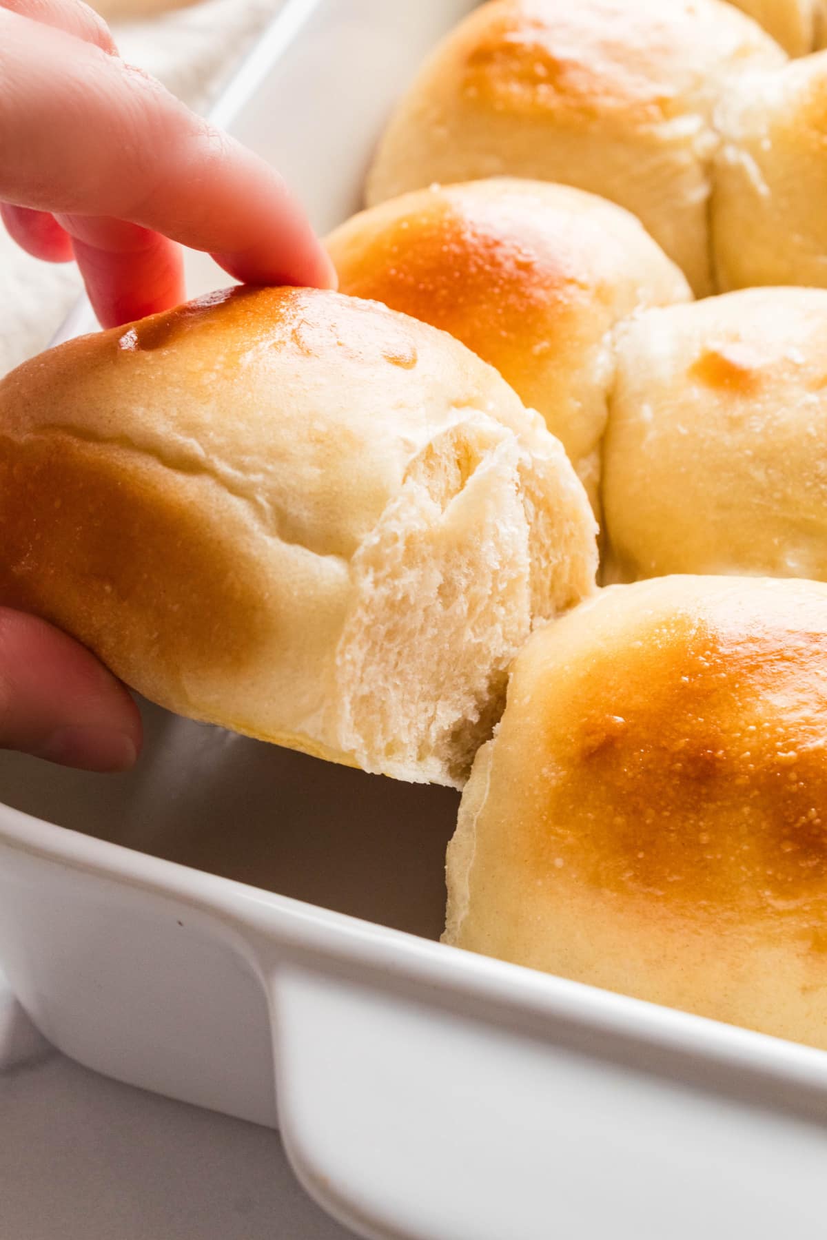 Soft pull-apart roll with a tender interior Hand pulling a soft dinner roll from the baking dish to reveal its tender interior.