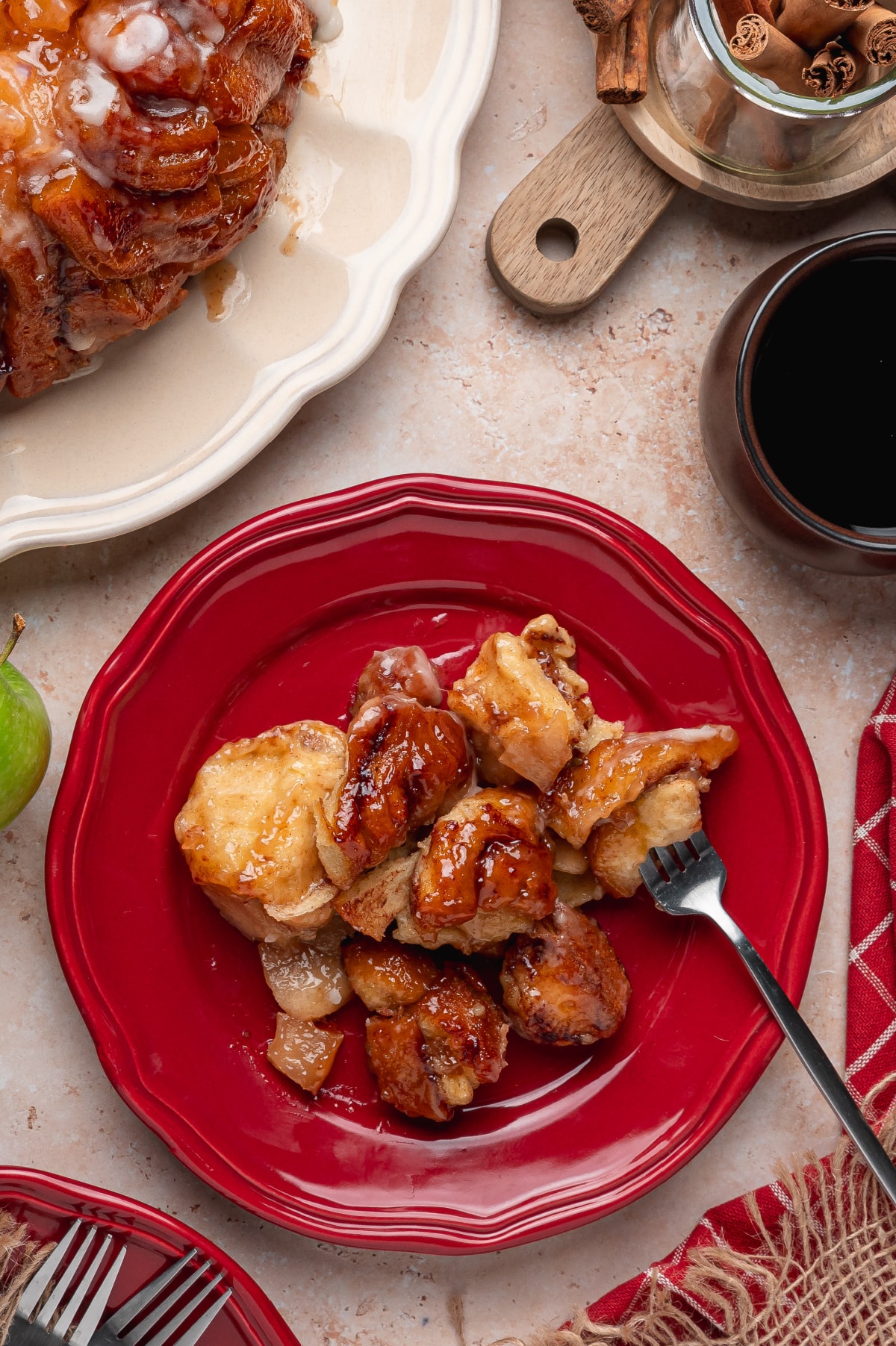 Warm Apple Monkey Bread with Cinnamon Rolls Warm cinnamon roll monkey bread pieces with apple pie filling and brown sugar sauce served on a red plate.
