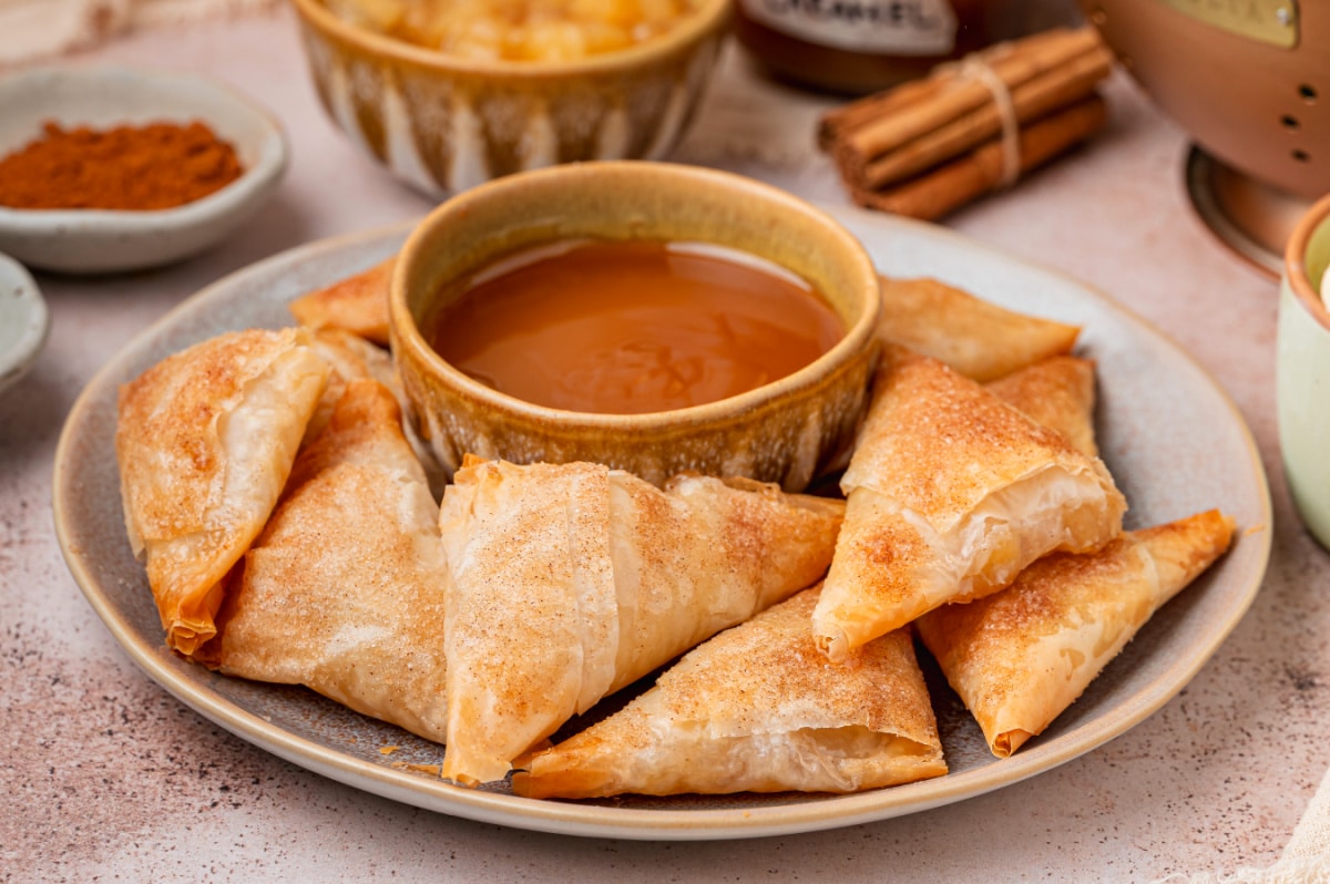 Cinnamon Sugar Apple Pie Samosas Cinnamon sugar apple pie samosas arranged on a plate with caramel sauce for dipping.