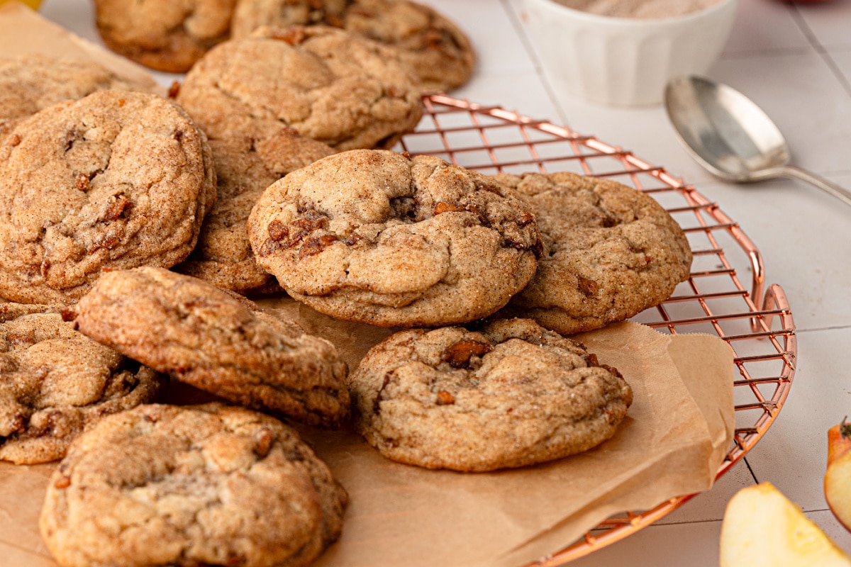 Cinnamon sugar apple snickerdoodle cookies with pieces of cooked apple throughout the soft dough. Soft and chewy apple snickerdoodles cooling on a wire rack