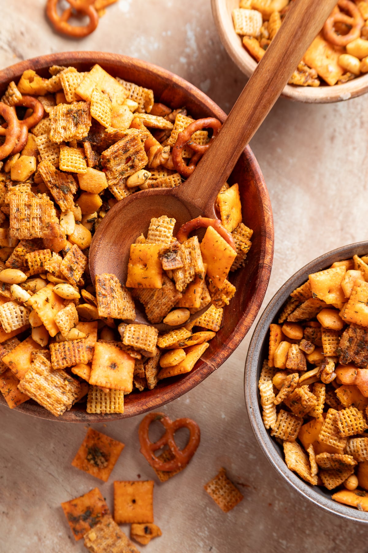 Seasoned Chex mix with crisp crackers, pretzels and nuts served from a wooden spoon. Baked Chex mix with Cheez-It crackers, Triscuits, pretzels, peanuts and walnuts served in wooden bowls