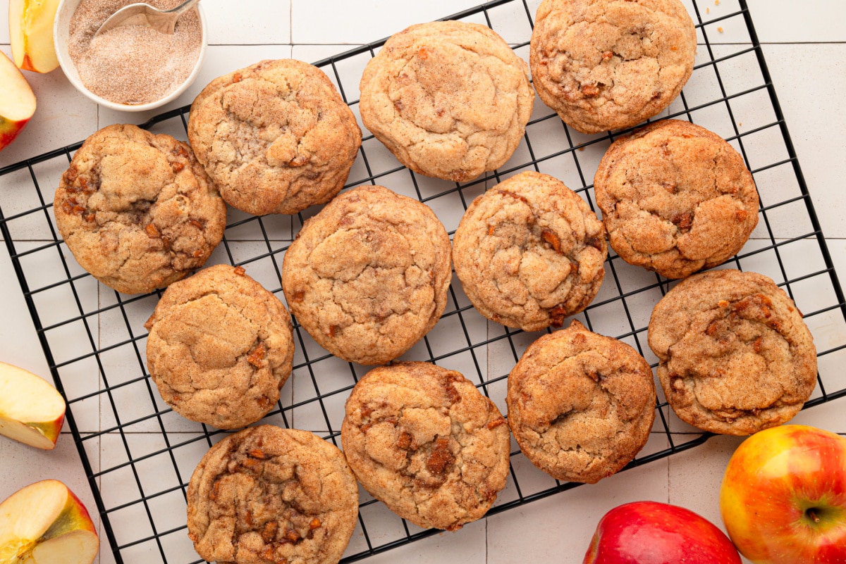 Thick, soft snickerdoodle cookies made with cinnamon-spiced apples and finished with cinnamon sugar. Cinnamon apple snickerdoodle cookies with cooked apple pieces cooling on a wire rack