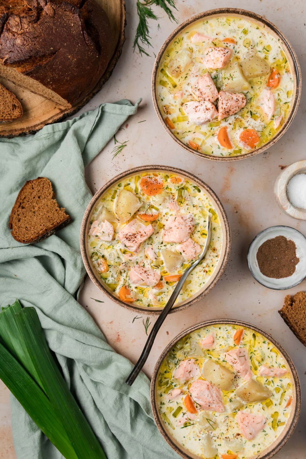 Finnish salmon soup served with dark bread, with chunks of salmon and potatoes in a creamy dill broth. Three bowls of Finnish salmon soup with salmon, potatoes, carrots, leeks and fresh dill served with dark bread.