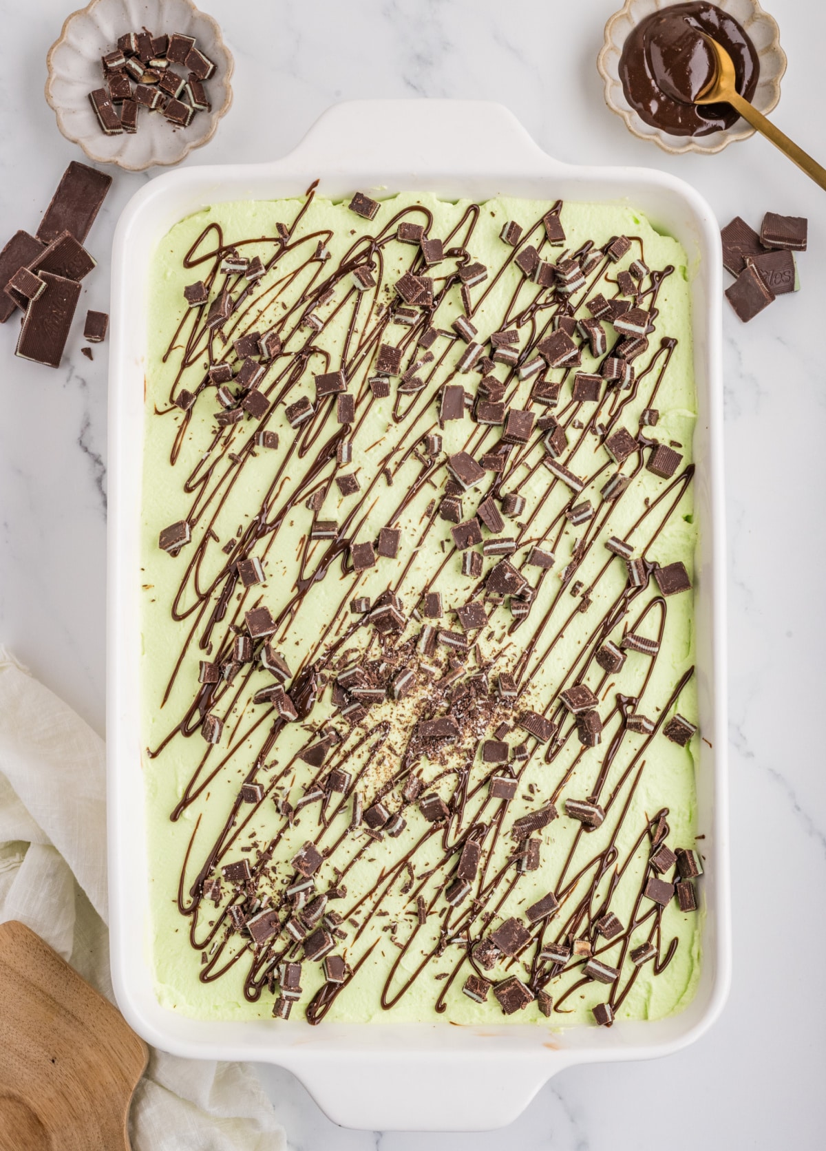 Andes Mint Chocolate Poke Cake with Whipped Cream Finished chocolate poke cake in a 9×13-inch baking dish topped with pale green mint whipped cream, chopped Andes mints and hot fudge drizzle.