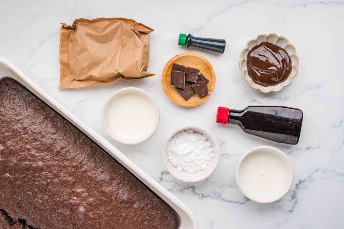 Ingredients for Chocolate Mint Poke Cake with Andes Mints Ingredients for chocolate mint poke cake including baked chocolate cake, hot fudge sauce, pudding mix, milk, heavy cream, powdered sugar, mint extract, green food coloring and Andes mints.