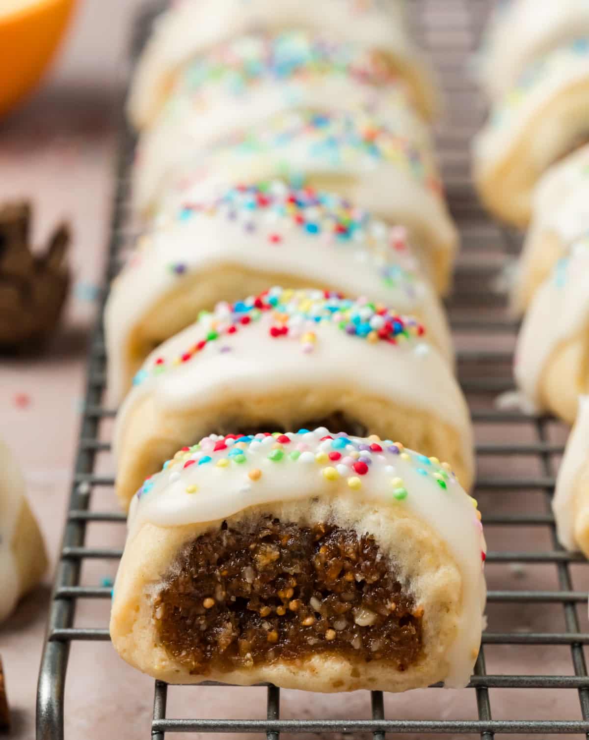 Cuccidati Cookies with Fig, Date and Walnut Filling Close-up of a cuccidati cookie showing moist fig, date, and walnut filling inside tender orange-scented pastry, topped with vanilla glaze and rainbow sprinkles.