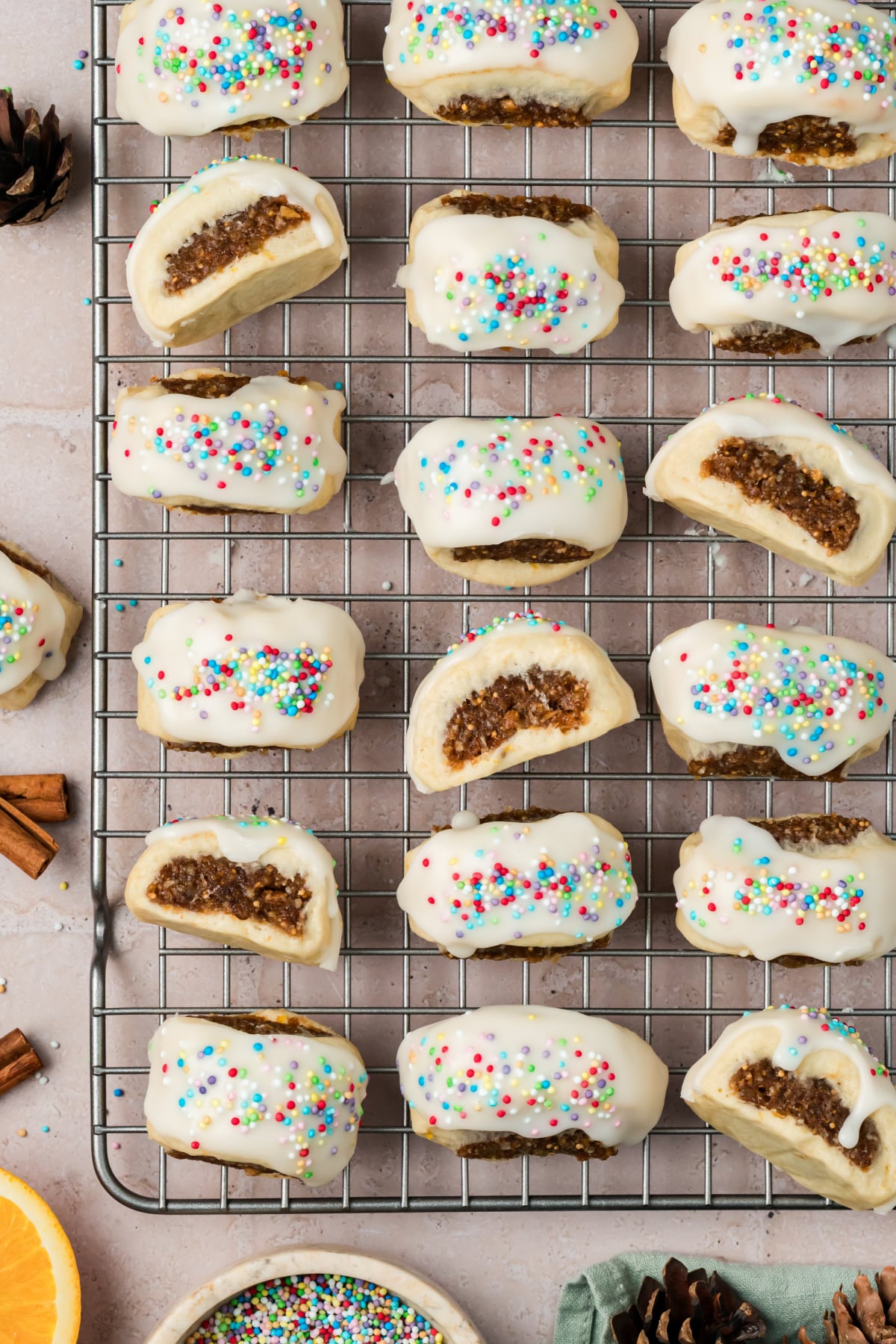 Glazed cuccidati cookies arranged on a wire cooling rack, showing colorful rainbow nonpareils, white vanilla icing, and exposed fig filling. Glazed cuccidati cookies arranged on a wire cooling rack, showing colorful rainbow nonpareils, white vanilla icing, and exposed fig filling.