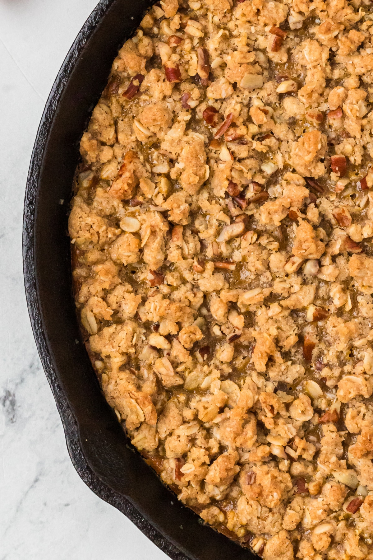 Close-up of golden brown oat and pecan crisp topping baked in a cast-iron skillet.