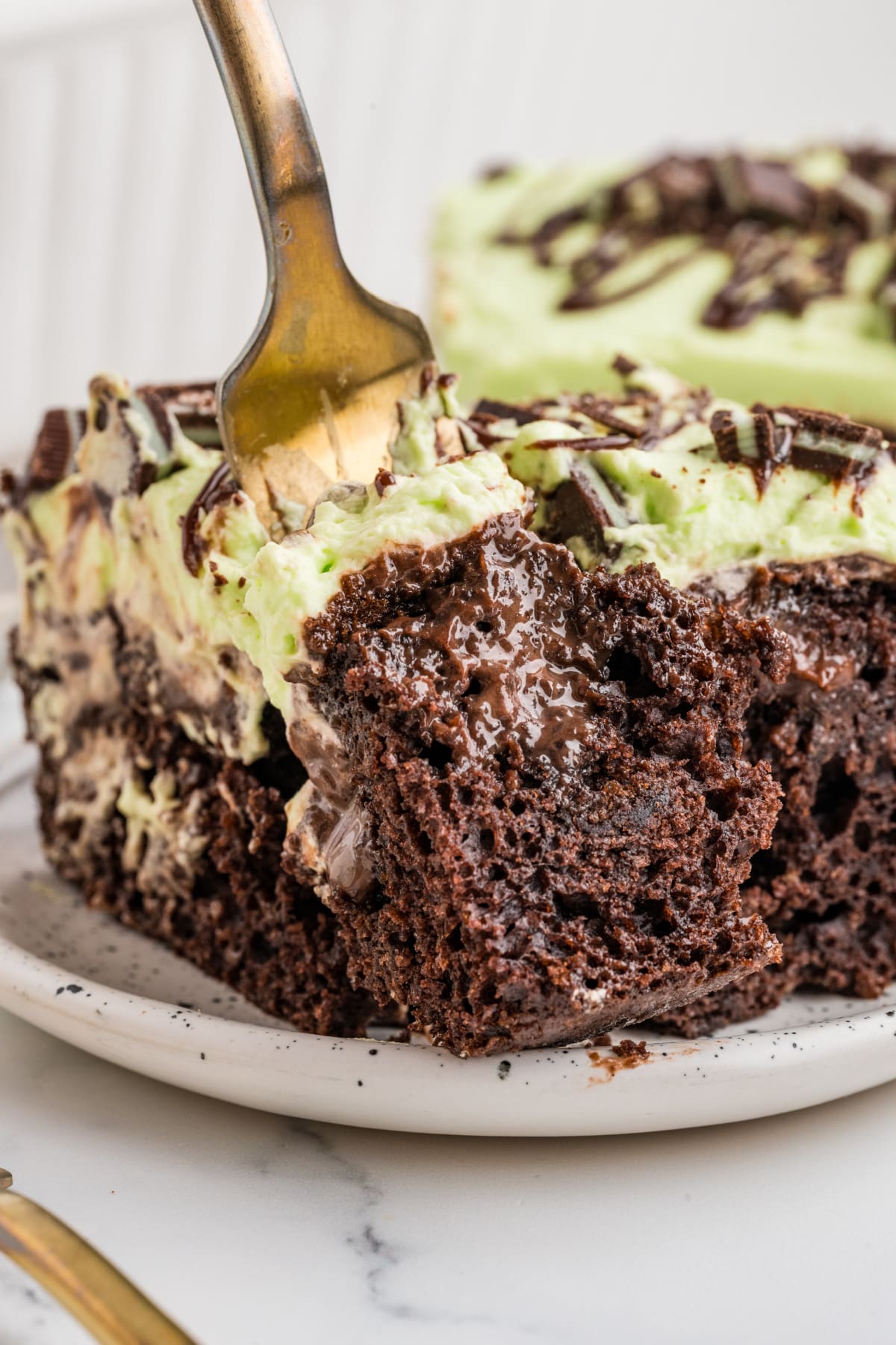 Mint Chocolate Poke Cake with Hot Fudge and Mint Whipped Cream Mint chocolate poke cake with gooey hot fudge filling, pale green mint whipped cream and a fork lifting a bite.