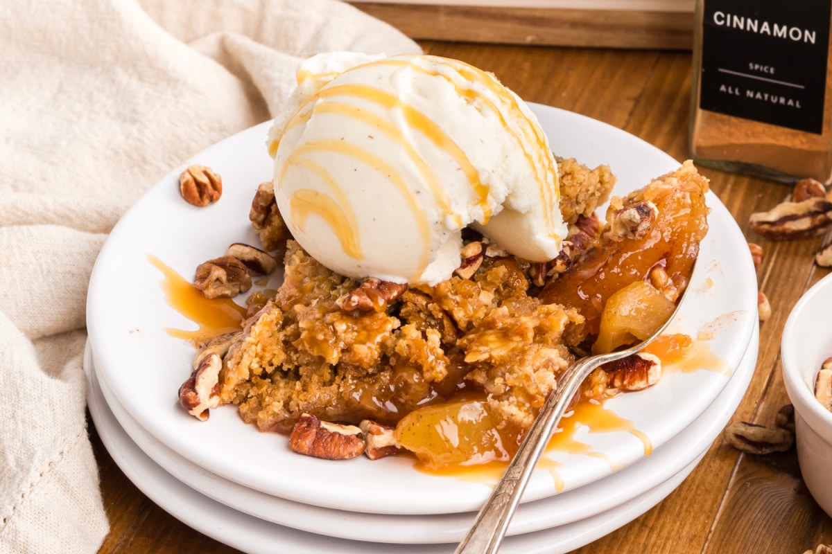 Oatmeal cookie apple crisp dump cake served with vanilla ice cream, caramel drizzle, chopped pecans, and cinnamon apple filling.