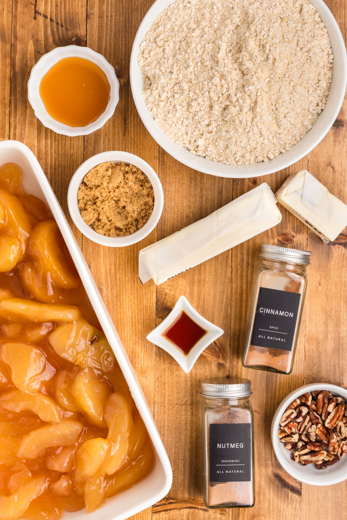 Ingredients for oatmeal cookie apple crisp dump cake, including apple pie filling, oatmeal cookie mix, butter, brown sugar, spices, pecans, and caramel sauce.