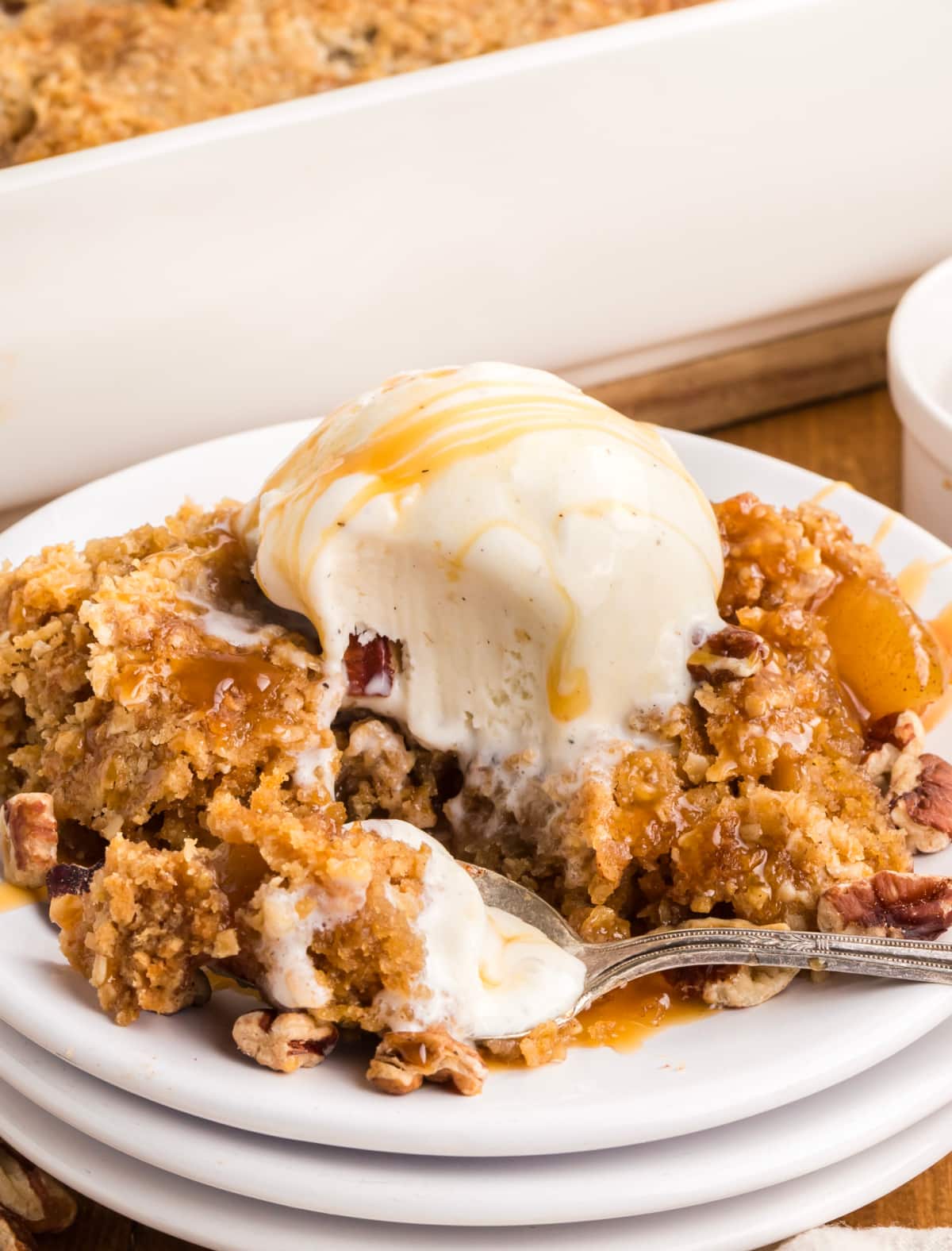 Spoonful of oatmeal cookie apple crisp with melting vanilla ice cream, caramel sauce, chopped pecans, and cinnamon apples.