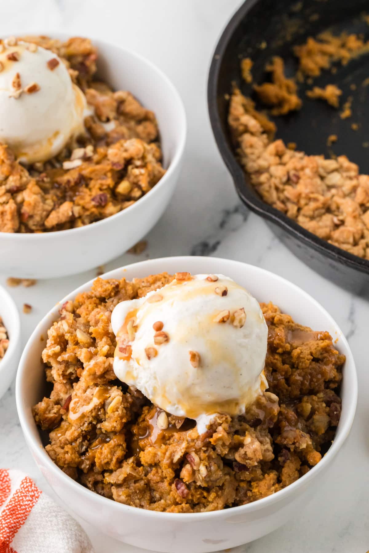 Pumpkin crisp with oat and pecan topping, vanilla ice cream, and caramel sauce served in a white bowl.