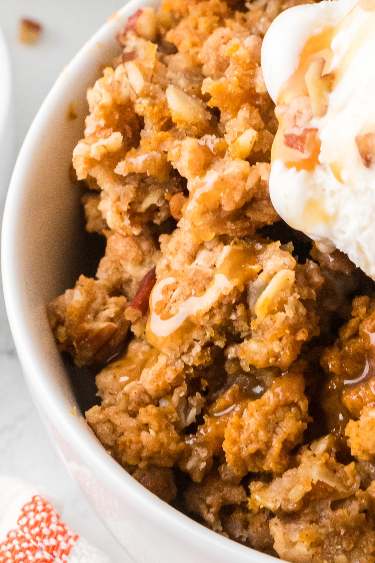 Close-up of creamy pumpkin custard with buttery oat and pecan clusters, caramel sauce, and vanilla ice cream.