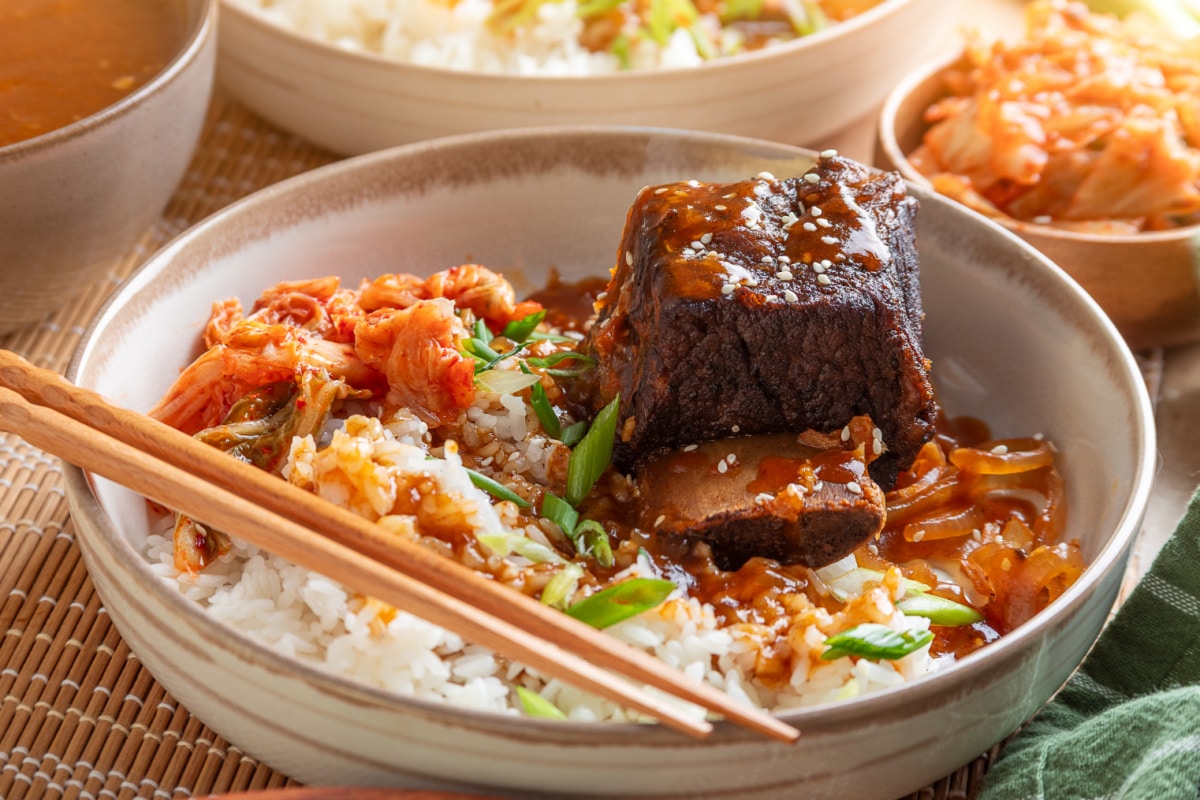 Slow Cooker Korean Short Ribs Served with Rice and Kimchi Bone-in Korean short rib coated in gochujang sauce, served over white rice with kimchi, softened onions, and green onions.
