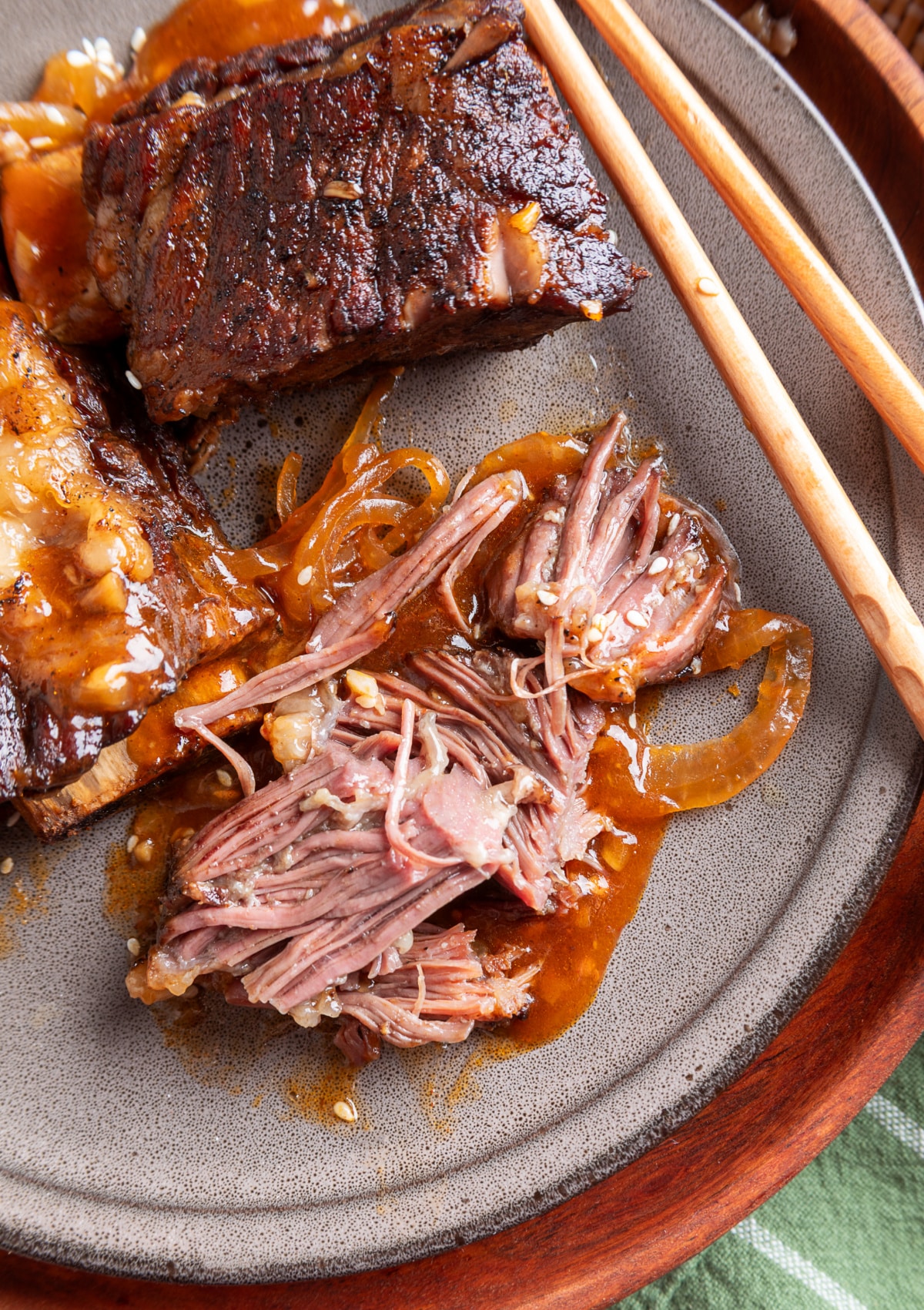 Slow Cooker Beef Short Ribs with Tender Meat and Gochujang Sauce Fork-tender beef short ribs pulled apart on a gray plate with softened onions and gochujang sauce.