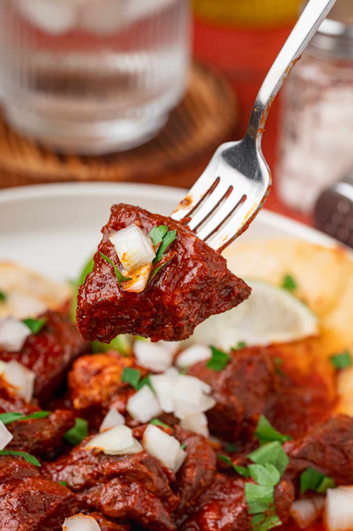 Fork-Tender Pork Shoulder in Red Chile Sauce Fork holding a tender piece of pork shoulder coated in red chile sauce